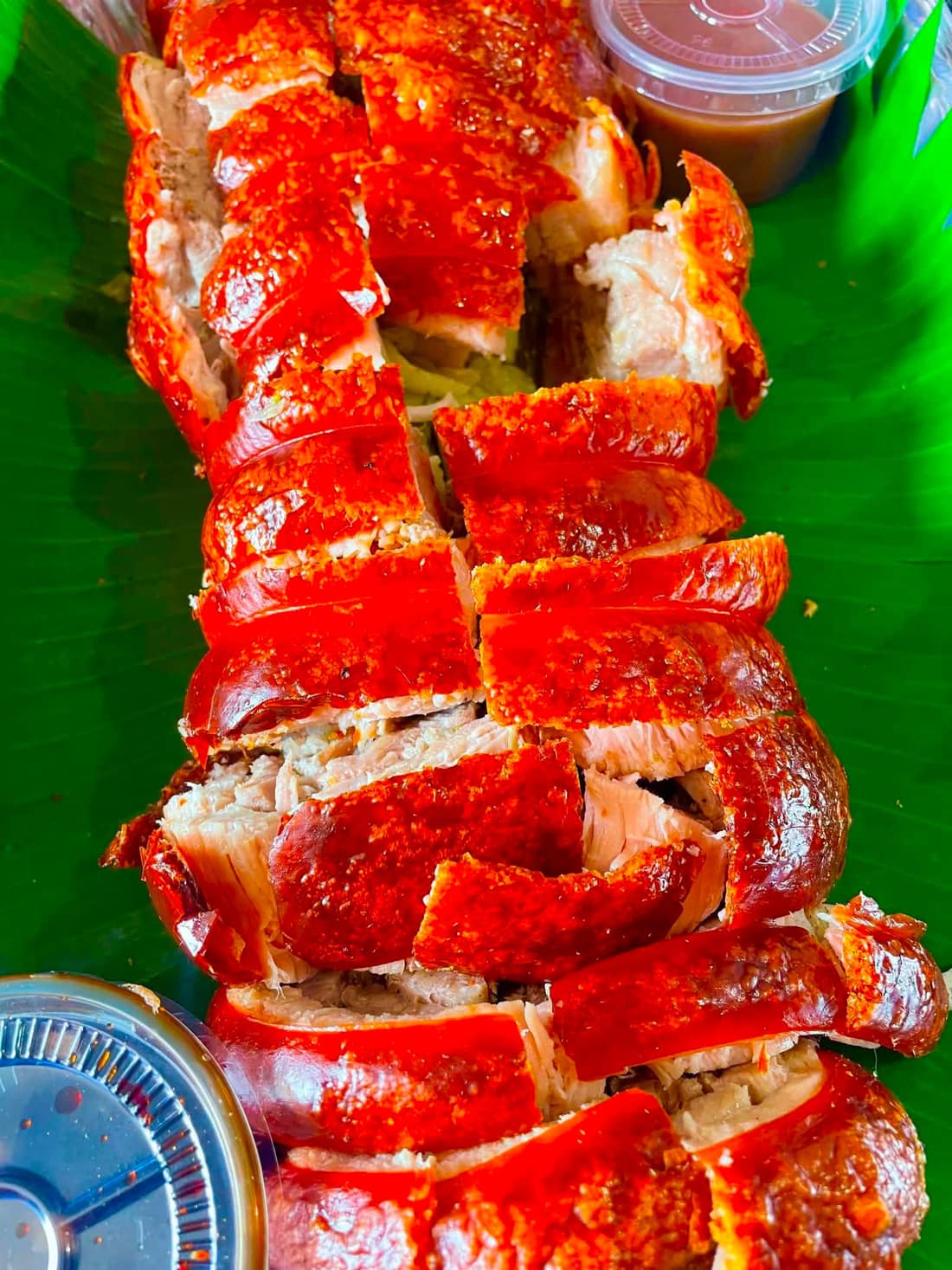 Flame-roasted pork belly lechon on a wooden board with dipping sauce